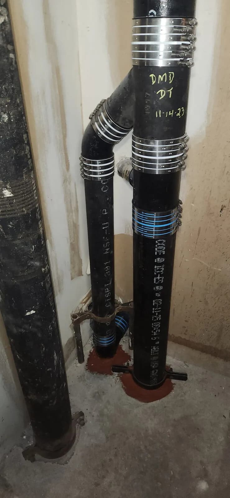 Cast iron drain stack with no-hub couplings and red firestop sealant at a concrete floor