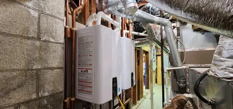 Two wall-mounted tankless water heaters with copper piping and PVC venting in a mechanical room