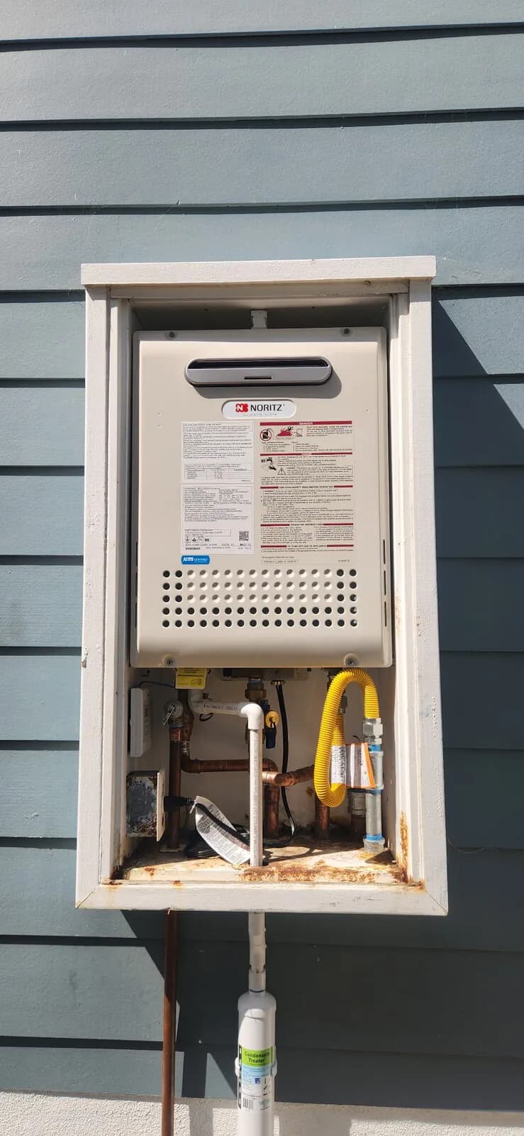 Noritz tankless water heater installed in a recessed outdoor wall box with copper and gas connections