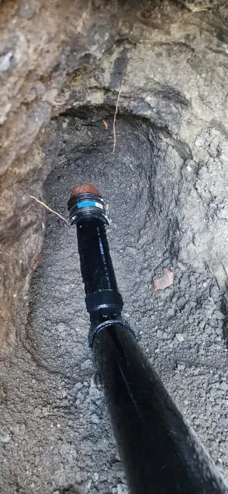 Sewer repair joining new black ABS pipe to older clay pipe with a rubber coupling in a trench