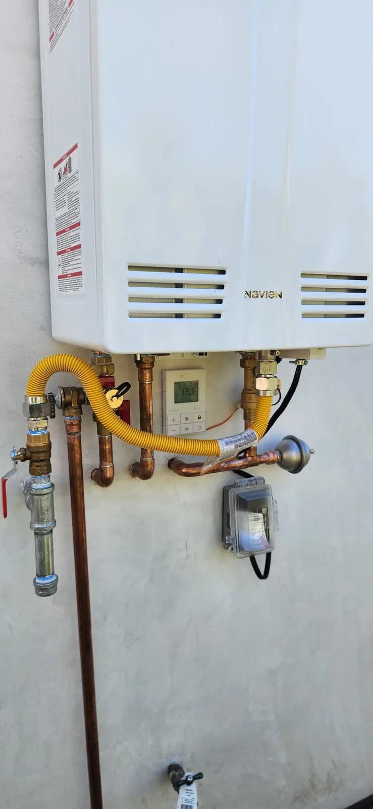 Navien tankless water heater on a stucco wall with yellow gas flex and copper piping